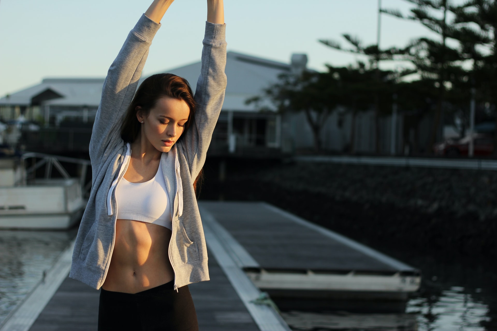 Woman stretching with arms up wearing white crop top and black pants